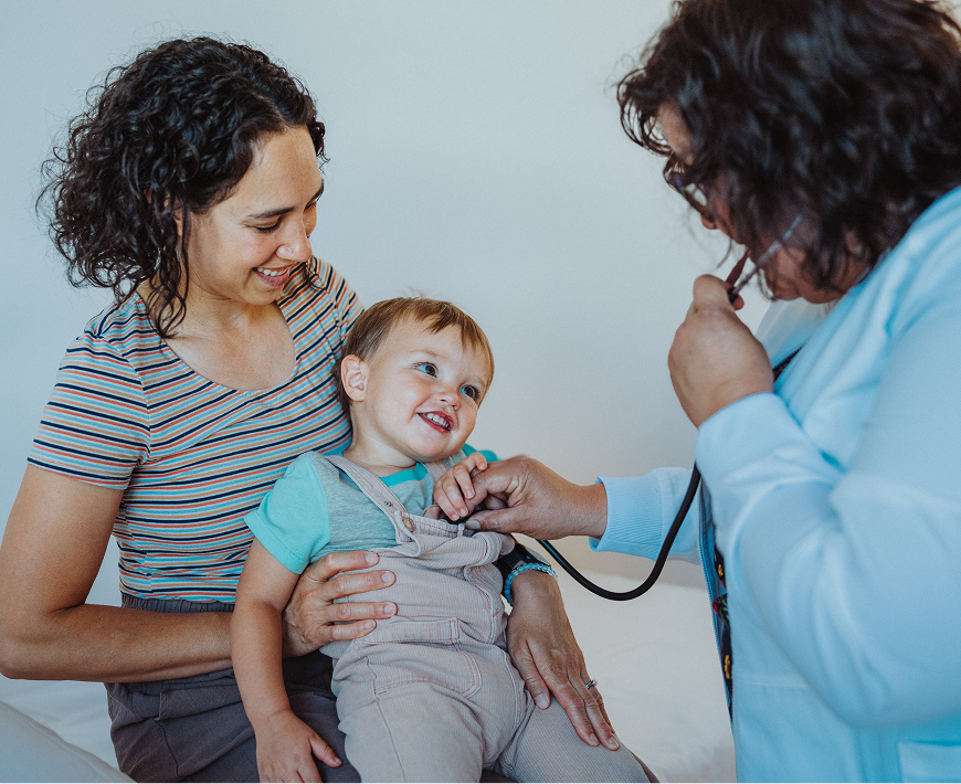 Pediatrician using stethoscope on smiling toddler.