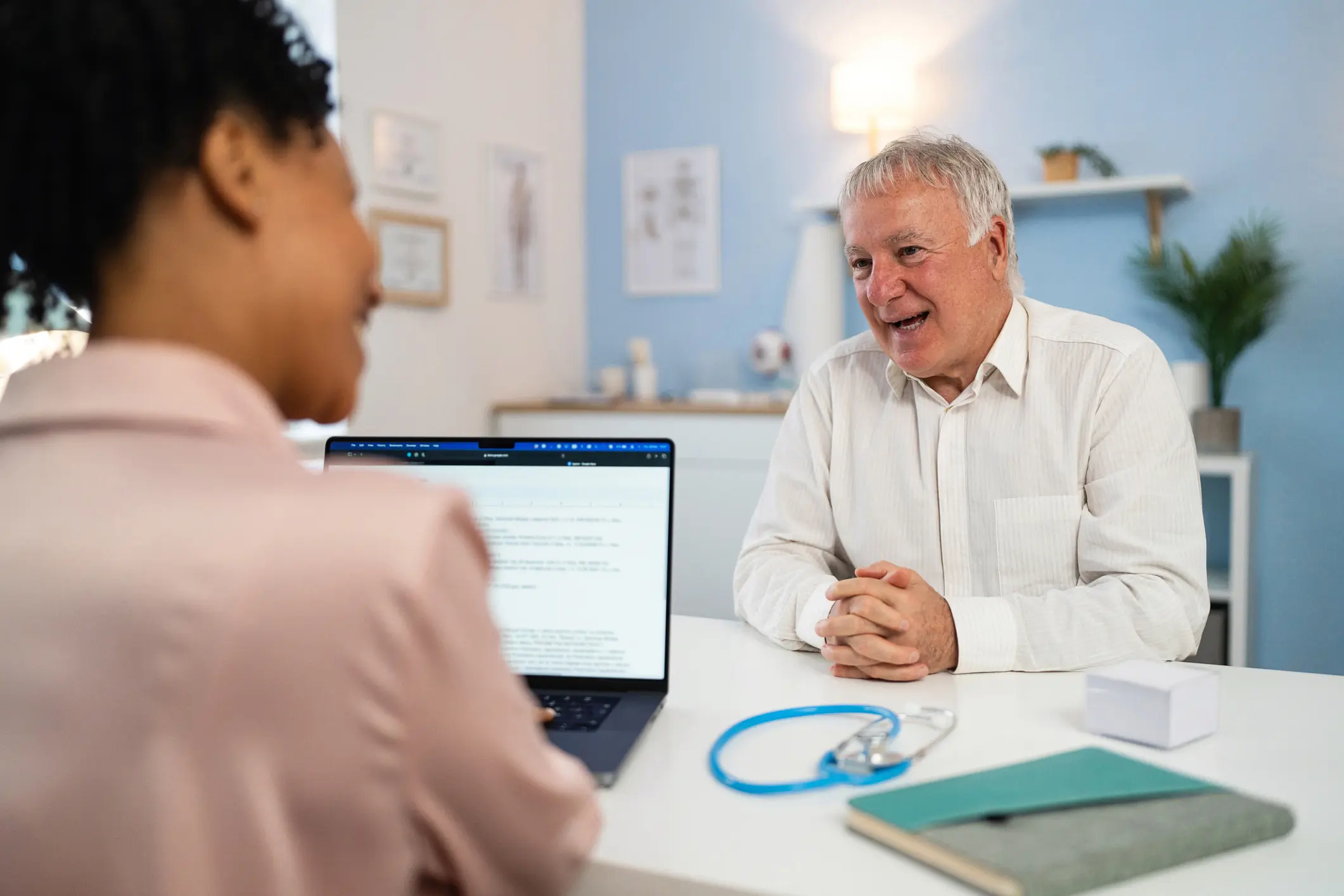 Senior Caucasian male patient, having an annual medical check-up with a female doctor Black ethnicity, at the modern ordination