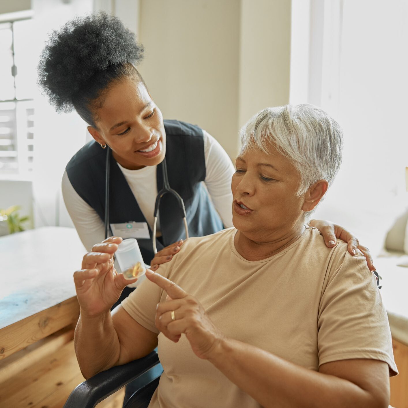 Elderly patient, caregiver and talking about pills for healthcare in a nursing home. Senior woman with a nurse for healing, medicine and advice or rehabilitation in a wheelchair with health insurance