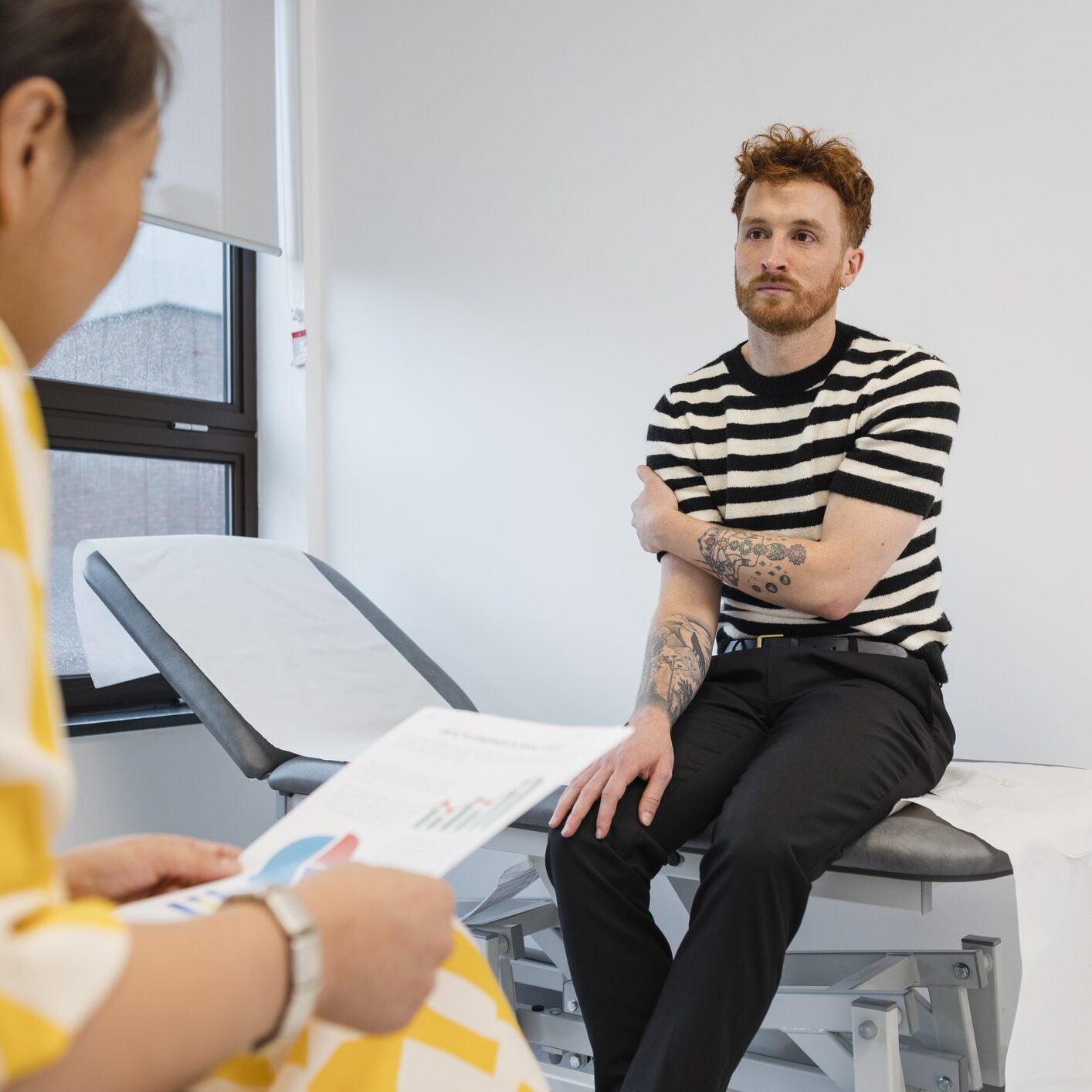 A medium close up of a female doctor who is making notes about a patients shoulder and trying to work out what sort of muscular damage has been done as the patient is complaining of a stiff shoulder. She is advising him stretching exercises to help loosen his shoulder and how to not cause as much pain. She is conducting her examination in her clinic in Newcastle Upon Tyne in the North East of England.